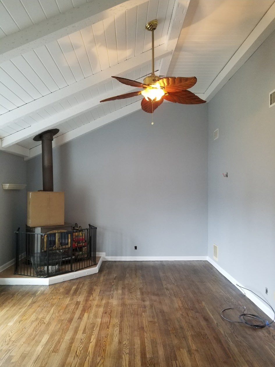 Vaulted living room in pale blue-grey with a ceiling fan and wood stove